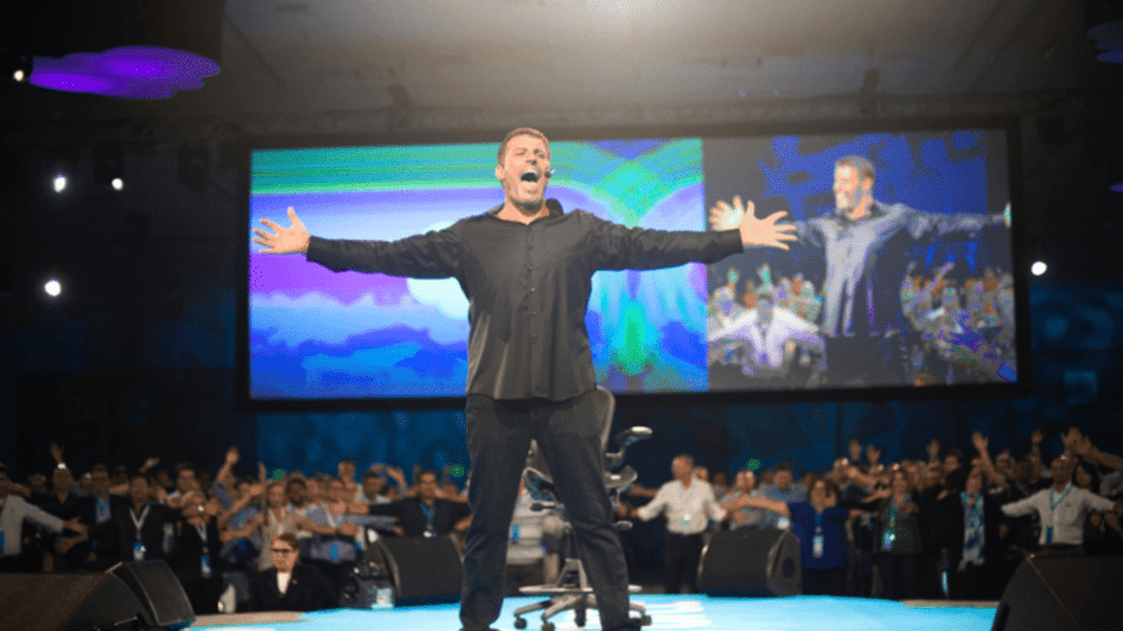 Tony Robbins at a seminar with his arms spread out wide chanting
