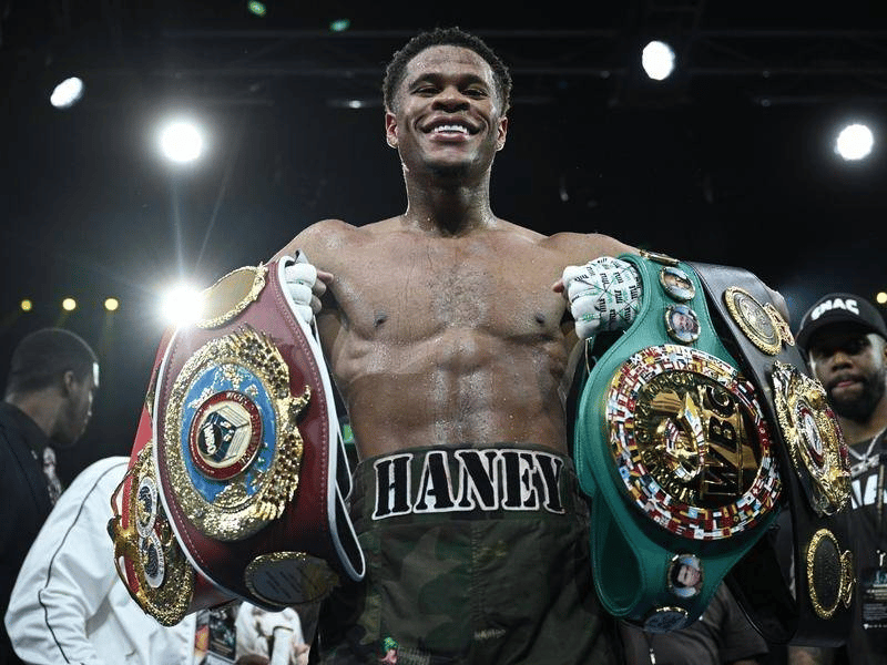 Devin Haney undisputed champion holding 4 belts in boxing ring